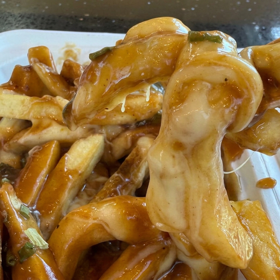 Golden fries topped with brown gravy and melted cheese are served in a white takeout container.
